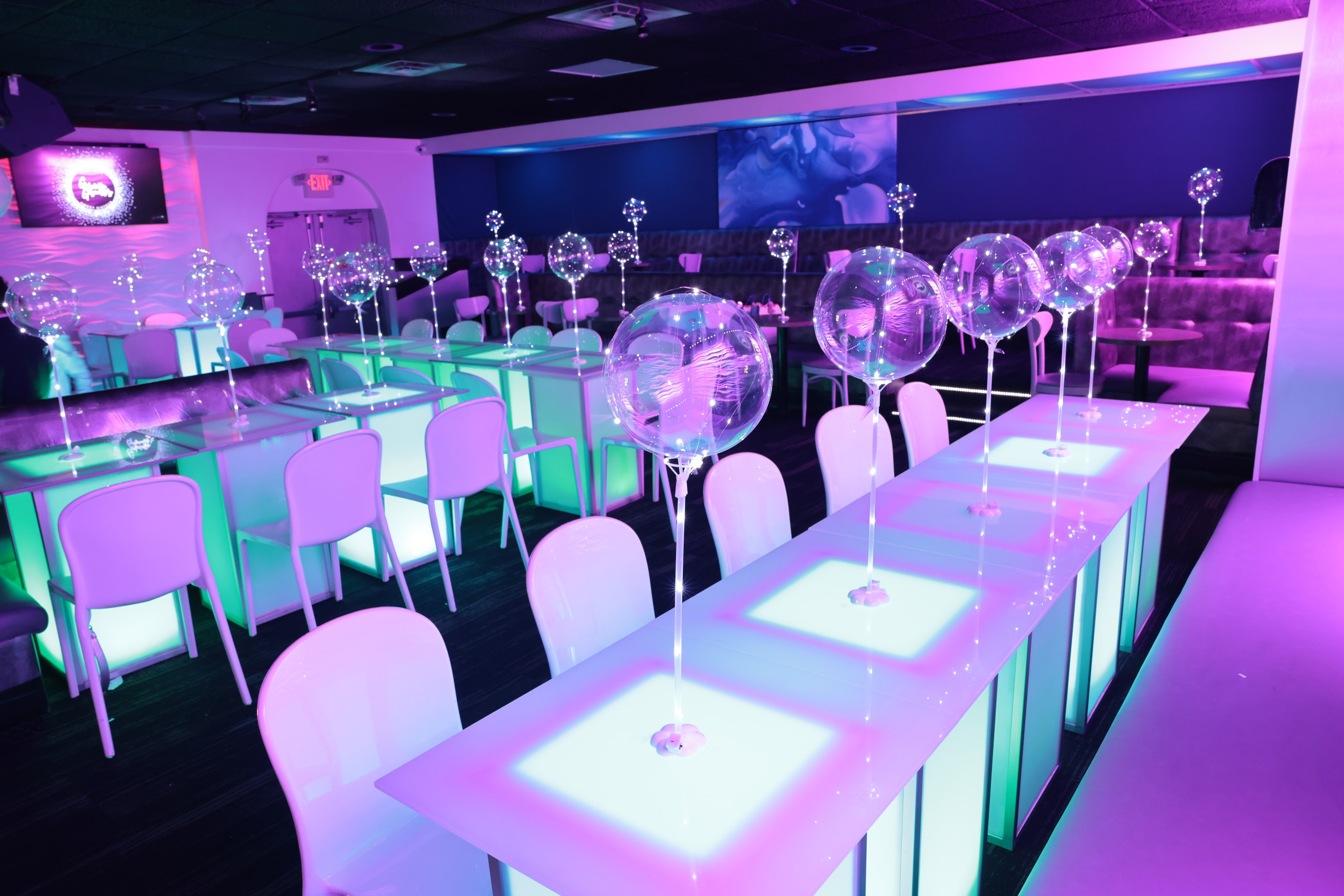A party room arranged with illuminated tables and balloons